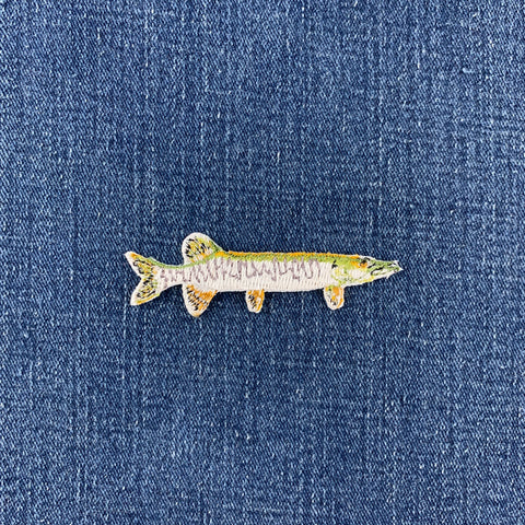 A realistic fish-shaped patch featuring a detailed pattern of green, brown, and gray scales, isolated on a denim background.