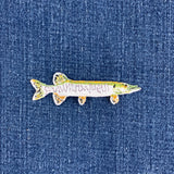 A small fish-shaped patch with a white body, green and yellow markings, and orange accents, placed on a blue denim background.