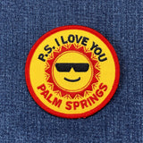 A round patch with a design that includes a sun wearing sunglasses and the text 'P.S. I LOVE YOU PALM SPRINGS'