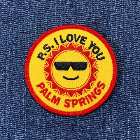 A round patch with a design that includes a sun wearing sunglasses and the text 'P.S. I LOVE YOU PALM SPRINGS'