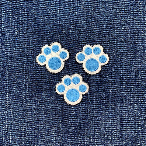 Three blue paw print patches on a denim background