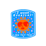 A sticker with a tan background and a cartoon sun character wearing sunglasses. The text on the sticker reads 'I WORK EVERYDAY (ON THIS TAN)' surrounded by pink stars against a blue background.