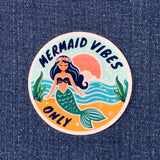 Round sticker with the text 'MERMAID VIBES ONLY' illustrated with a mermaid, sun and sea theme on a denim background.