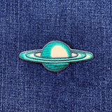 A patch depicting the planet Saturn with blue rings and a white core on a denim background