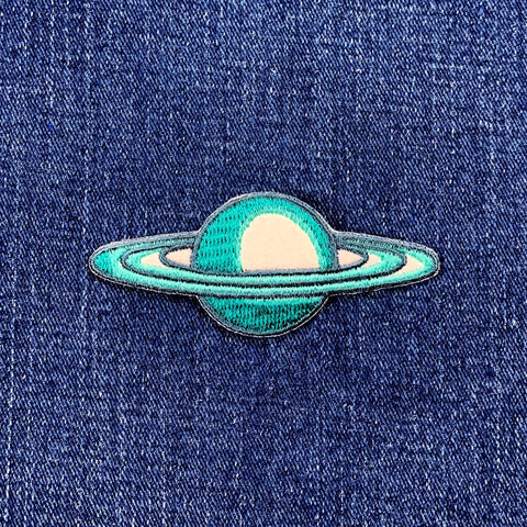 A patch depicting the planet Saturn with blue rings and a white core on a denim background