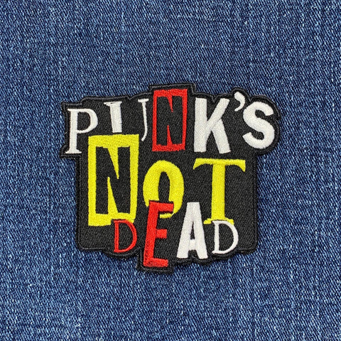 An applique patch with the text 'PUNK'S NOT DEAD' in a bold, graphic style, displayed on a denim background
