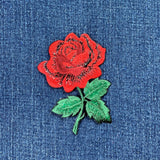 red rose patch with green leaves and stem, and shimmery threads, displayed on a denim background