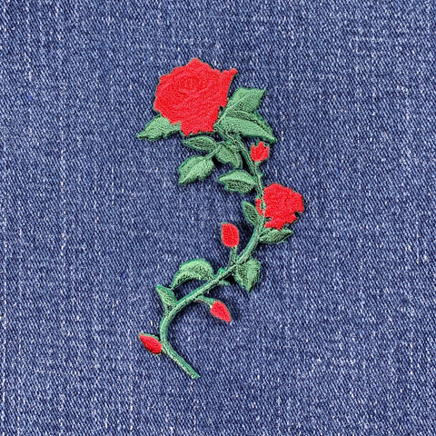 A medium-sized red rose applique patch with green leaves and buds, on a denim background