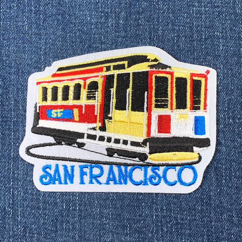 Embroidered patch shaped like a red, yellow, and black San Francisco cable car, with the name 'SAN FRANCISCO' stitched below it.
