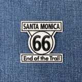 Embroidered patch with the text 'Santa Monica 66 End of the Trail' and the number 66 in a circular design, a sign found on Route 66 in California.