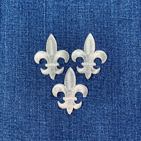 Three silver fleur-de-lis patches on a blue denim background