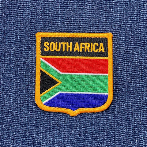 an embroidered patch of the South Africa flag in the shape of a shield on a denim background