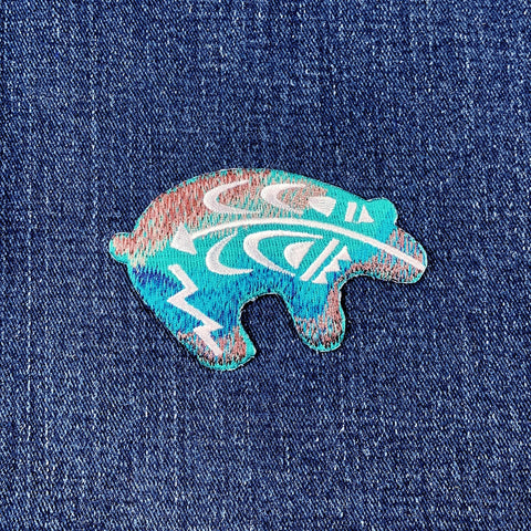 A embroidered Southwest bear applique patch in blue and green colors on a denim background