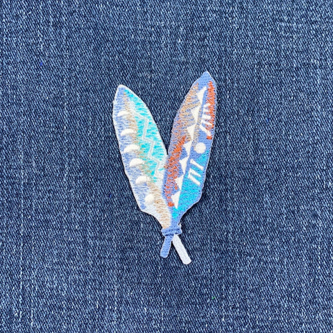 A colorful feather applique patch with Native American inspired design, displayed on denim fabric
