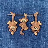 A patch with three embroidered monkeys hanging from a branch on a denim background