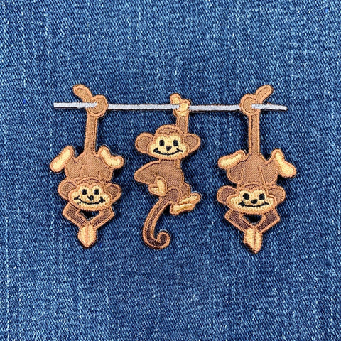 A patch with three embroidered monkeys hanging from a branch on a denim background