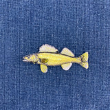 A small embroidered walleye fish patch in yellow and white, placed on a blue denim fabric background.