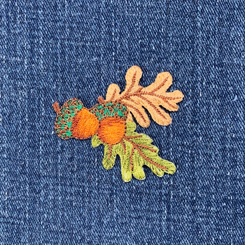 Embroidered patch depicting an acorn and oak leaves on a denim background