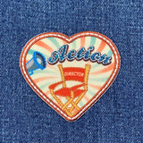 Heart-shaped patch with 'Action' and director's chair design on denim fabric