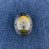 An oval enamel Walking Stick Medallion featuring the Alamo in San Antonio, TX, displayed on a blue denim fabric background.