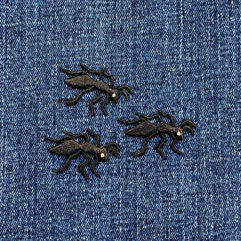 Three black embroidered ant patches on a blue denim fabric background