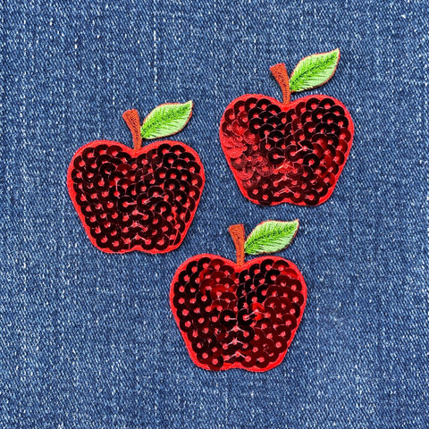 Three red sequin apple patches with green leaves on a denim background