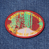 Oval embroidered patch depicting a winding road ("Avenue of the Giants") through towering redwood trees, with green leaves and orange-brown trunks. Text on the border names the region: "AVENUE OF THE GIANTS / REDCREST - MYERS FLAT - PHILLIPSVILLE"