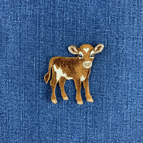 An embroidered baby cow patch on a blue denim fabric background.