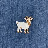 A small embroidered goat patch in white and tan, placed on a blue denim fabric background.