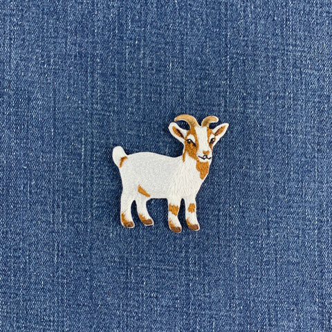 A small embroidered goat patch in white and tan, placed on a blue denim fabric background.