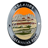 An oval enamel medallion featuring a landscape design of Badlands National Park. The pin has a polished silver-tone border with raised text reading 'BADLANDS NATIONAL PARK' at the top and bottom.