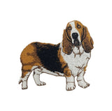 An embroidered patch of a Basset Hound dog, featuring its classic tricolor coat of brown, black, and white, isolated on a white background.