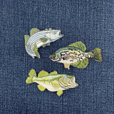Three embroidered fish patches on a denim background