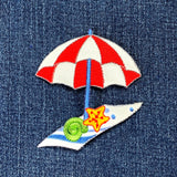 Embroidered patch of a red and white umbrella with a starfish and seashell on denim fabric.