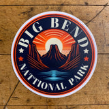 A round vinyl decal featuring a stylized sunset with mountains and the text 'BIG BEND NATIONAL PARK'.