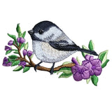 Embroidered patch of a bird on a branch with purple flowers on a white background
