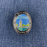 An oval metal enamel Walking Stick Medallion featuring the Biscayne National Park lighthouse design, placed on a blue denim background.