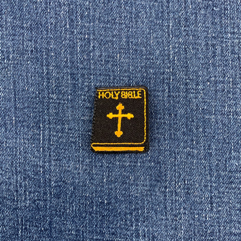 Embroidered patch of a 'Holy Bible' with a cross on blue denim fabric.