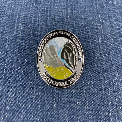 An oval metal medallion featuring the Black Canyon of the Gunnison National Park design, resting on a blue denim fabric background.