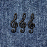 Three black embroidered G clef musical note applique patches on a denim background.