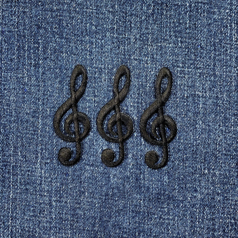 Three black embroidered G clef musical note applique patches on a denim background.