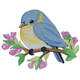 A embroidered patch depicting a bluebird on a branch with flowers, designed to be ironed onto fabric.