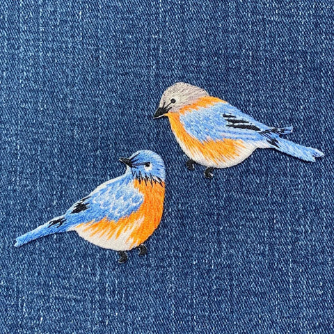 Two embroidered bluebirds on a denim background