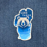Sticker in the shape of Lake Tahoe with a bear and 'Lake Tahoe' text on a denim background