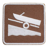 A square embroidered patch featuring a brown background with a white stitched boat and trailer graphic, surrounded by a white border.