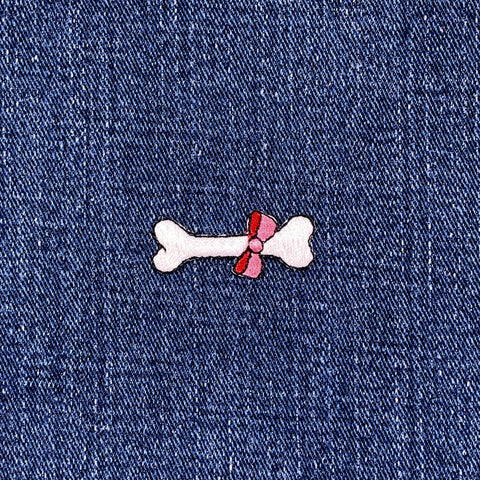 Bone-shaped patch with a pink bow on a denim background