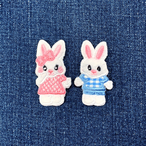 Two embroidered bunny patches, one in a pink dress and the other in a blue outfit, on a denim background.