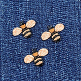 Three embroidered bumblebee patches with black and brown striped bodies on a blue denim fabric background.