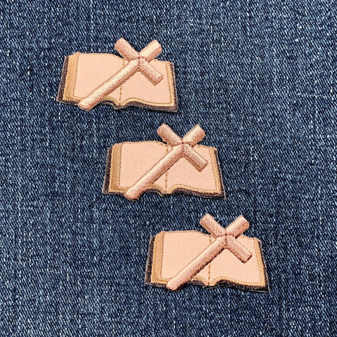 Three beige patches with a cross and bible design on a denim background