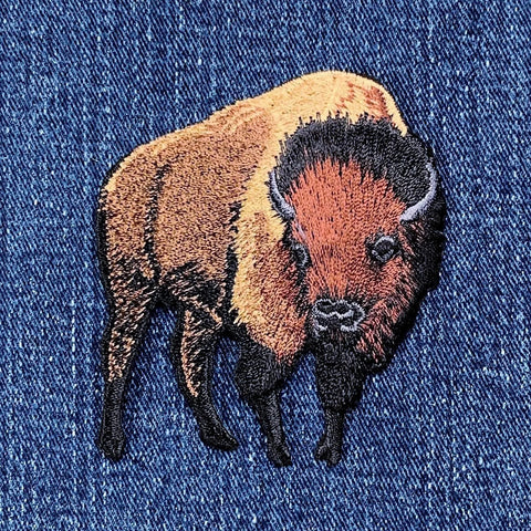 Embroidered buffalo applique patch with a brown, black, and beige design on a denim background.
